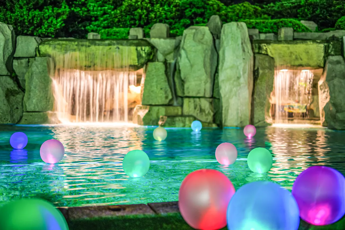 色とりどりの光る球体が水面に浮かび、ライトアップされた滝が美しい夜のプール