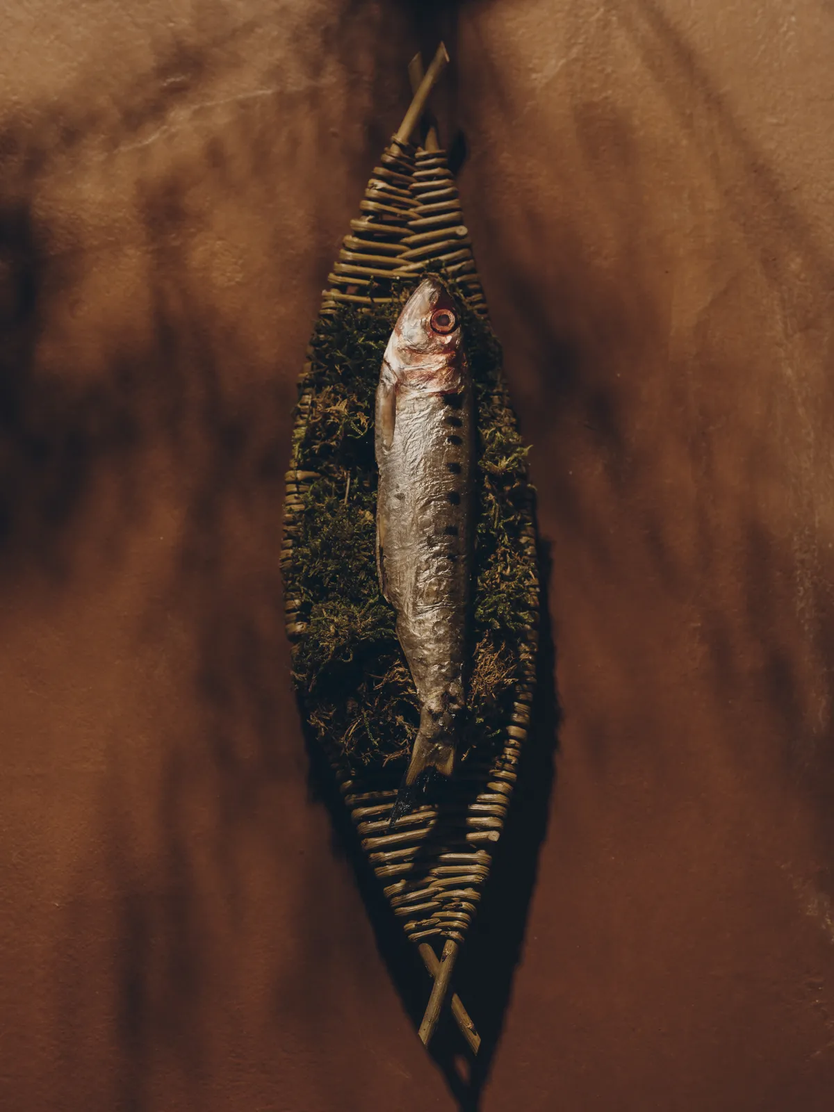 編み籠と苔の上に美しく盛り付けられた一匹の魚料理